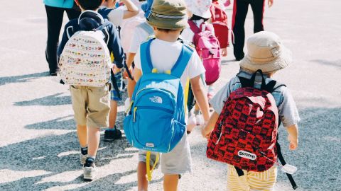 Young children carrying school backpacks, holding hands while crossing a road