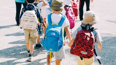 Young children carrying school backpacks, holding hands while crossing a road