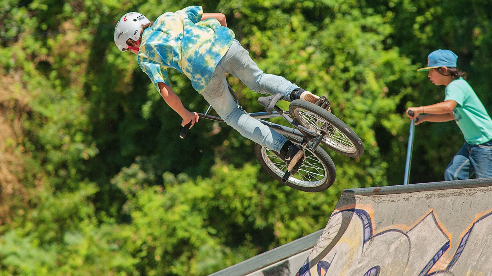 A young man riding a BMX bike in mid-air at a skate park banner image