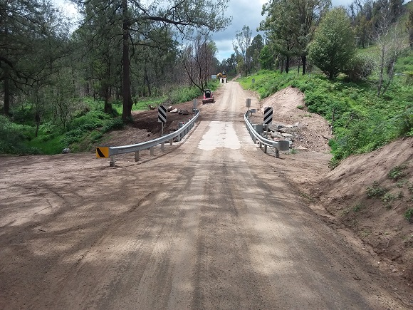 Image Guard rail lines both sides of a bridge on a straight dirt road