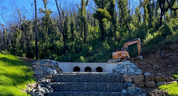 Image An excavator works above three concrete culverts positioned above gabion rock baskets