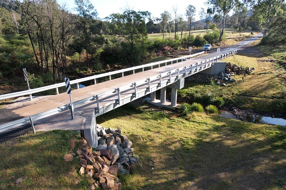 Image A new bridge crosses a narrow creek with grassed edges.