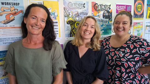 Three women standing in front of youth event posters on a wall