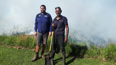 Two men standing with a shovel infront of smoking grass
