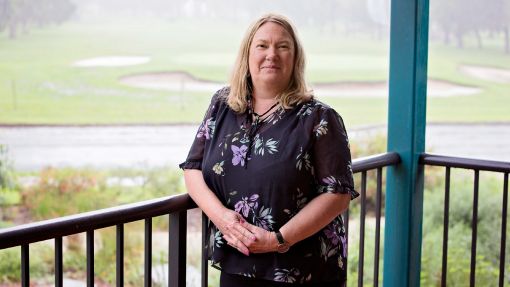 Fair-haired woman leaning against railing with golf course in background.