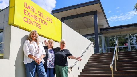 three women standing in front of sign saying basil sellers exhibition centre
