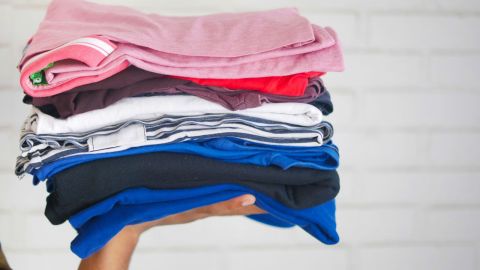 a hand holding up a small pile of folded t-shirts