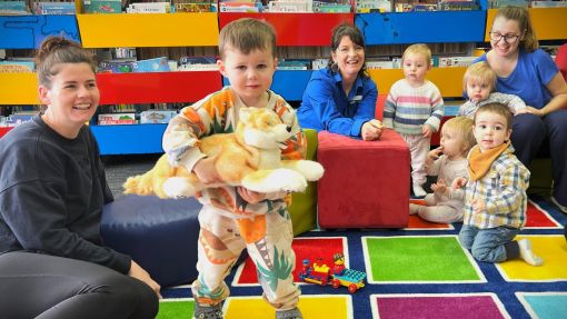 Robo dog being held by a young child during Rhymetime in the library.