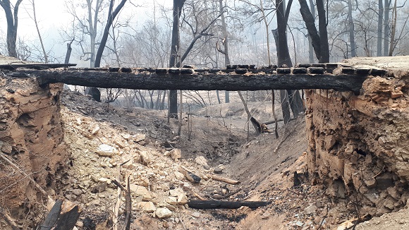 Image The bridge abutment walls no longer exist and the burnt girders straddle a dry creek bed