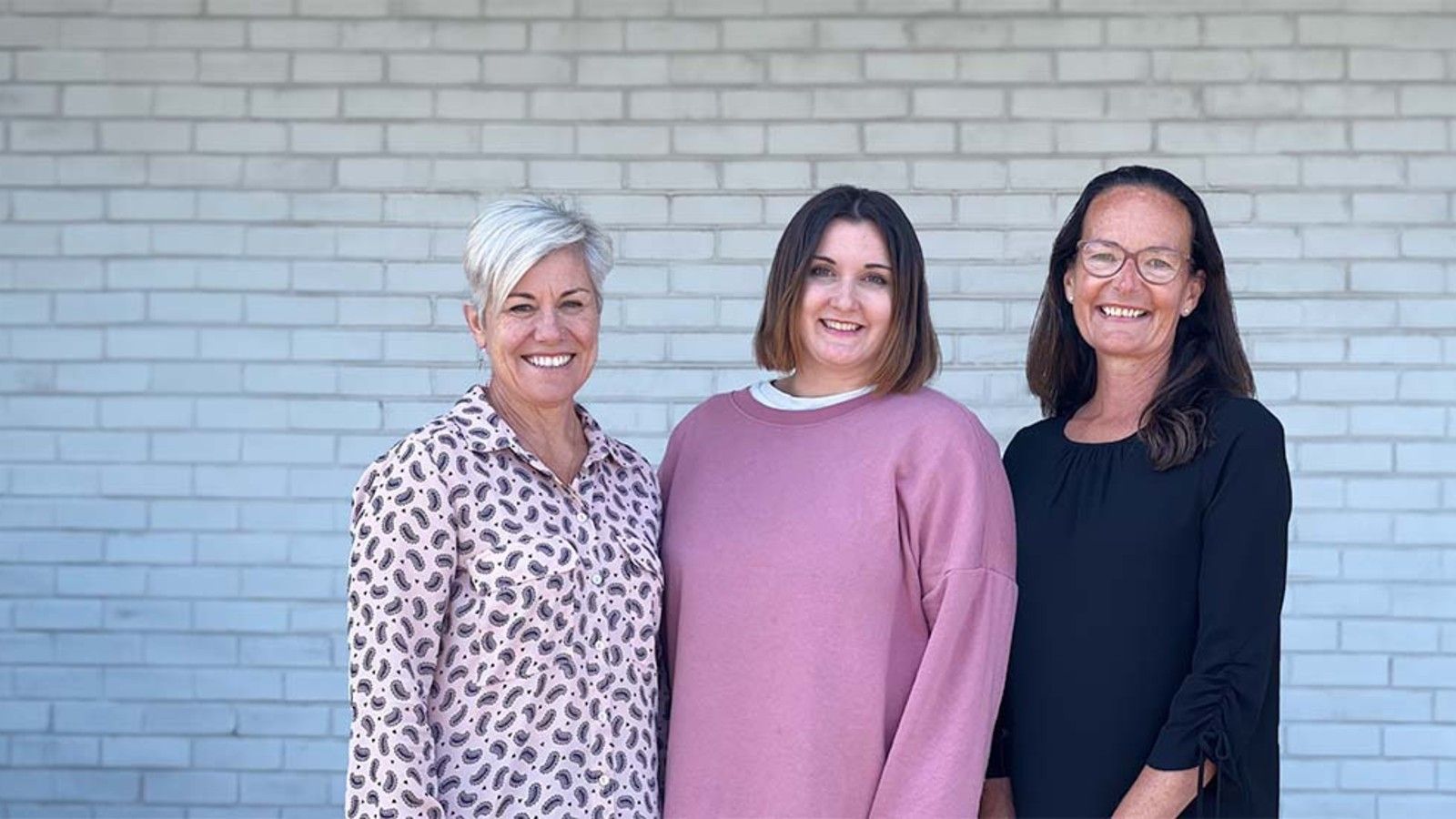 Three Job Shop staff members posed against a white brick wall. banner image