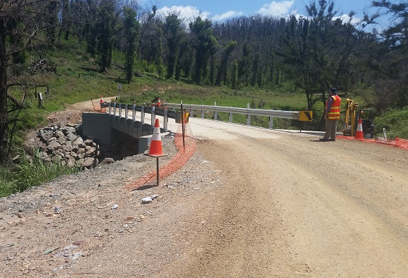 Image A new bridge with guardrail is positioned on a winding dirt road 