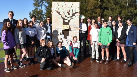 Students surround a collage of a tree with leaves noting changes to save the planet