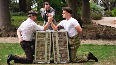 Two men arm wrestling on a stump with a man standing behind to judge