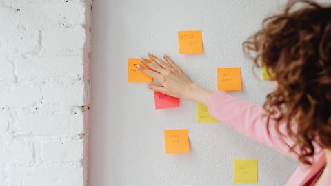 A person adding a post-it note to a wall displaying other post-it notes