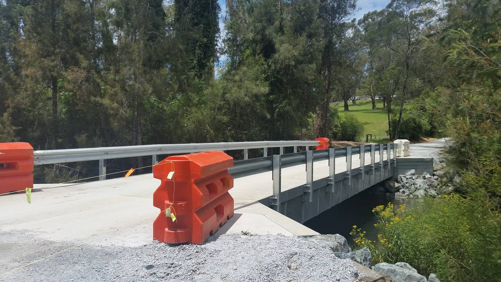 A concrete bridge lined with guardrail in a bushland setting.