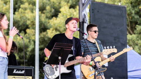 female and two males on stage singing with guitars