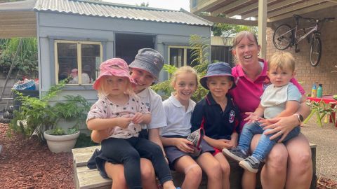 five children sitting with a woman in a backyard