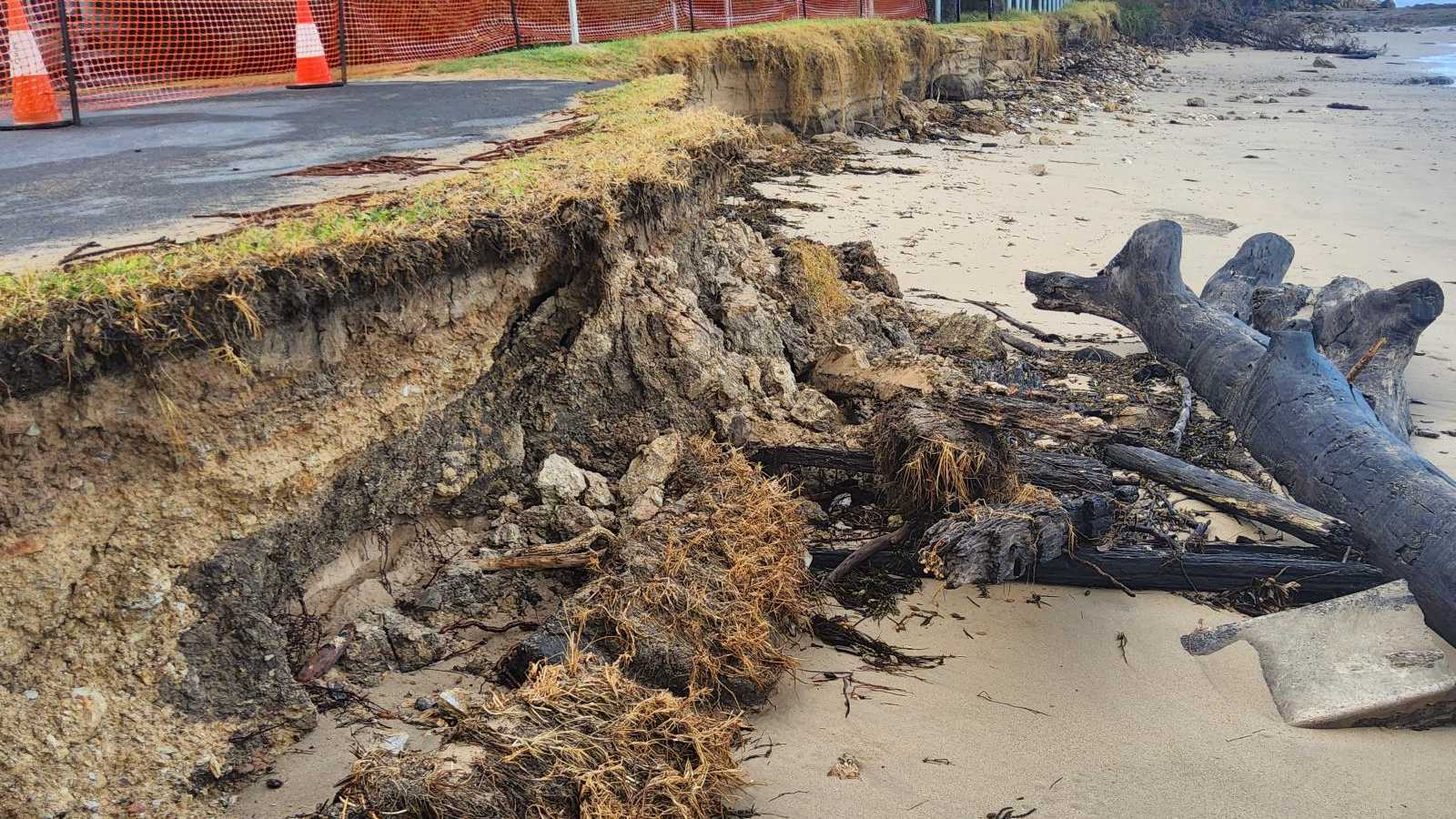 A narrow strip of grass remains between the road and an eroded drop off to the beach