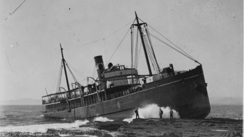 Image of a large working ship run aground on rocks.