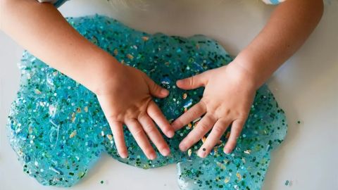 Child’s hands playing with blue glitter slime during a messy play activity.