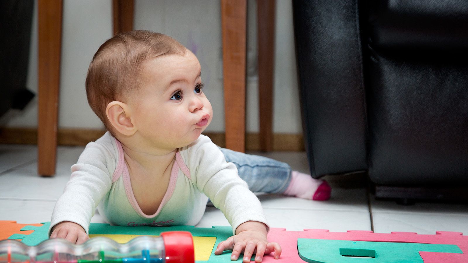 A baby on their tummy in front of brightly coloured toys banner image