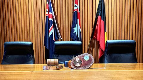 Council Chamber desk with gavel and clock with flags in the background.