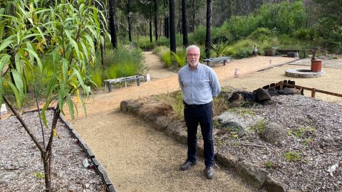 A man stands in a garden damaged by fire