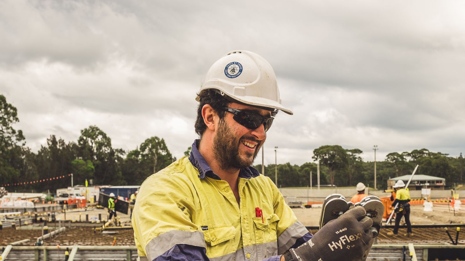 A construction worker at a large site, with more workers behind him banner image