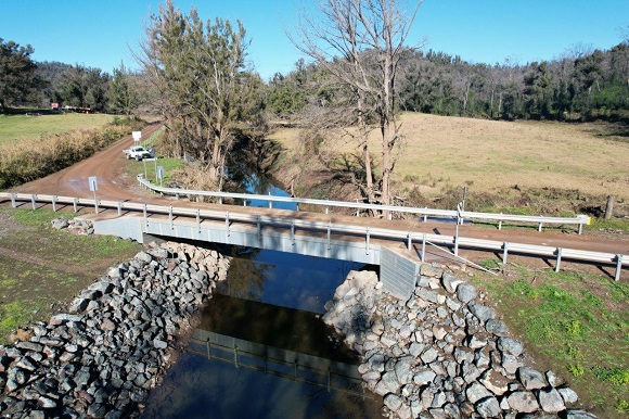 Image A bridge lined with guardrail crossed over a creek with a rocky embankment.. 