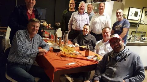 A group of men sitting and standing around a table smile at the camera. 