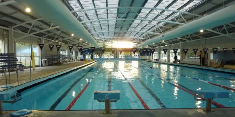 A long shot of an indoor swimming pool with one person swimming in one of the lanes.