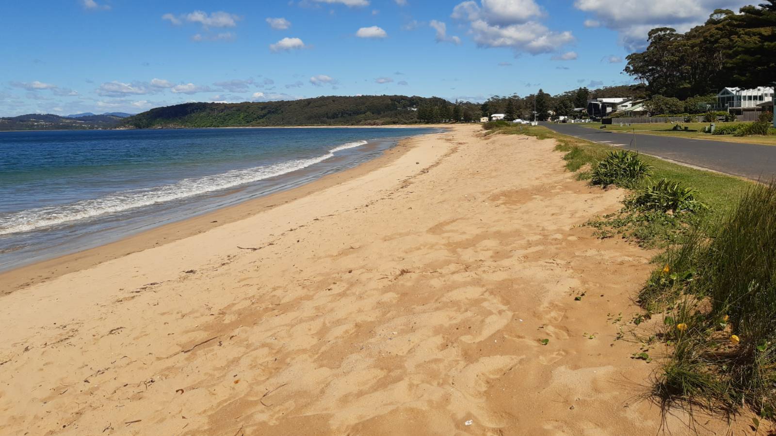 Image A bitumen road runs alongside a long sandy beach next to a calm sea.