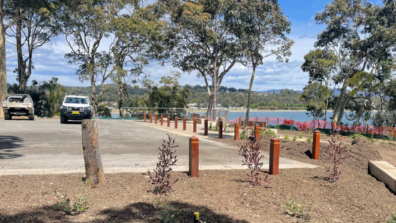 Image Timber bollards line a car park surrounded by gum trees overlooking the ocean.