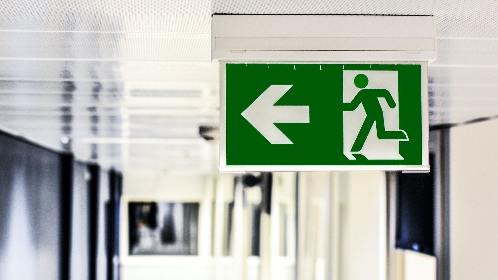 Green and white illuminated fire exit sign erected on a building ceiling banner image