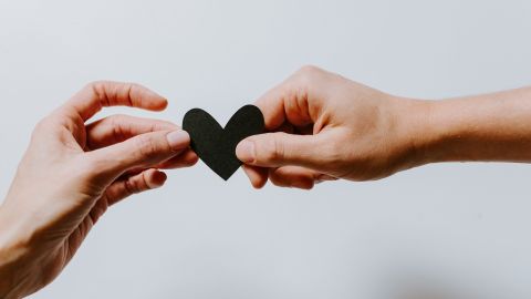 Two hands holding a small black heart.