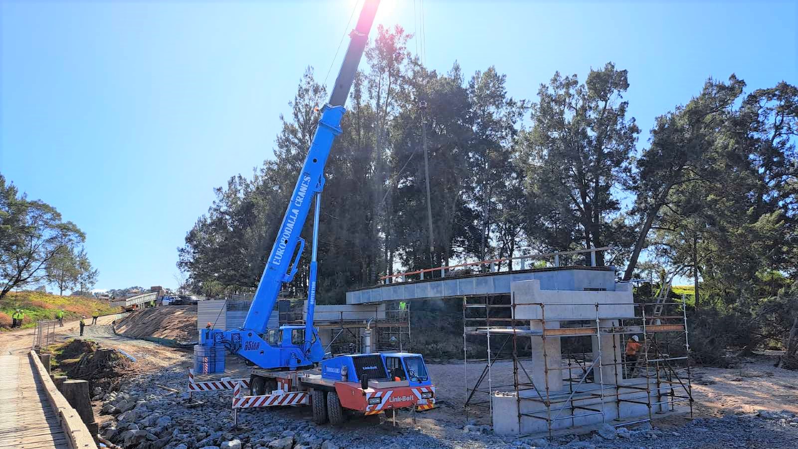 A mobile crane lowers a bridge deck section into place on a construction site.