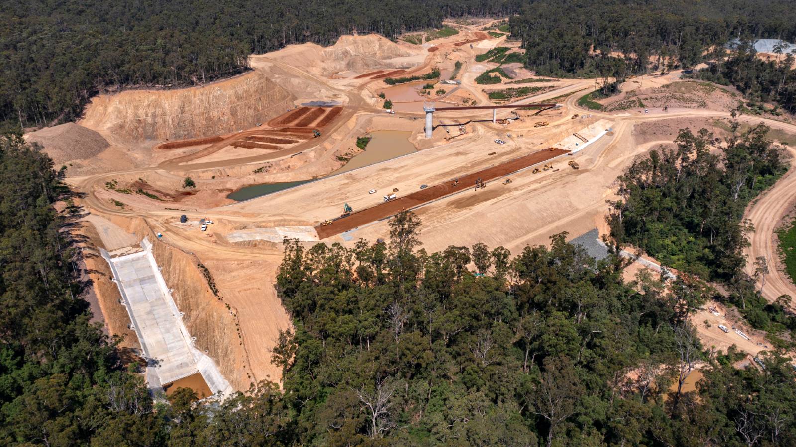 Bulk earthworks are underway on a large site surrounded by dense forest.