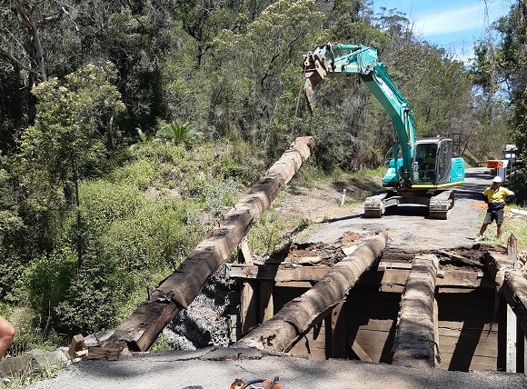 Image An excavator lifts a large timber bearer from the bridge