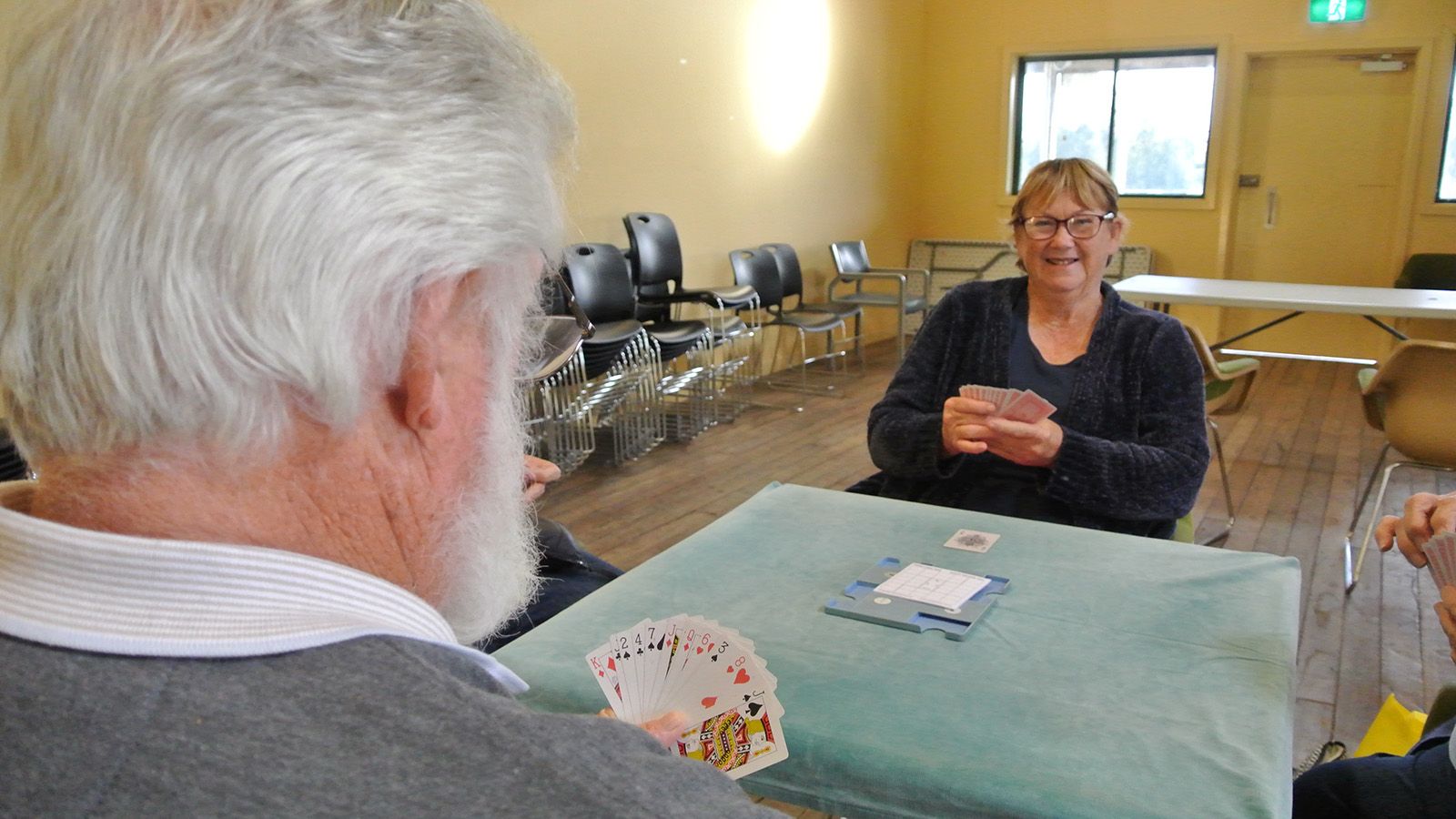A man and woman playing a card game on a green felt table banner image