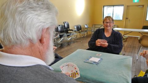 A man and woman playing a card game on a green felt table