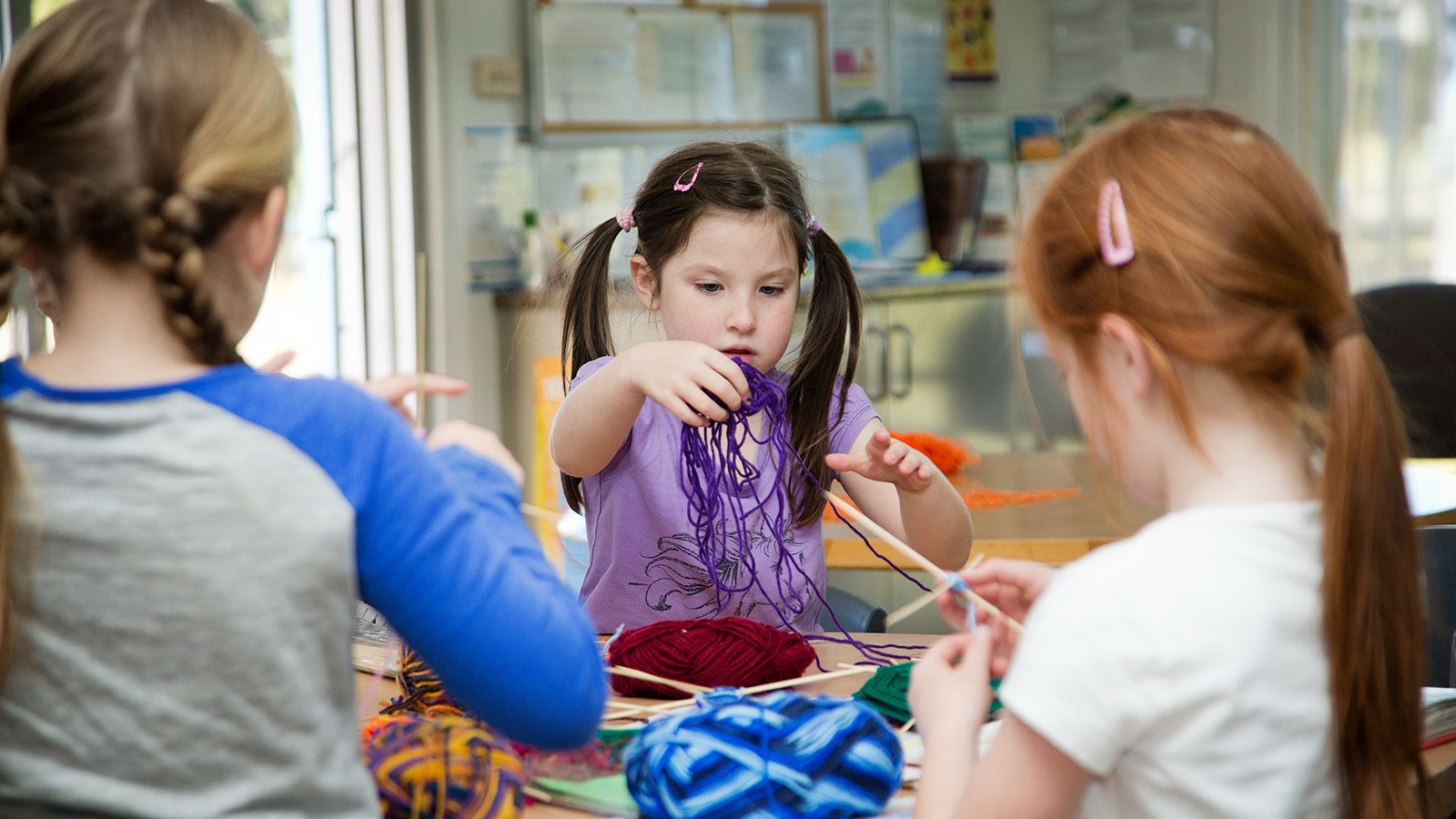 Three young girls participating in a craft activity with yarn banner image