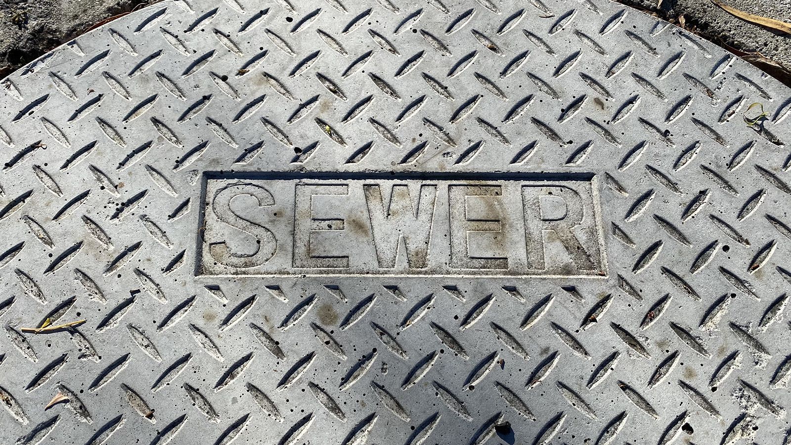 Metal cover of a sewer entry point marked with the word 'sewer' banner image