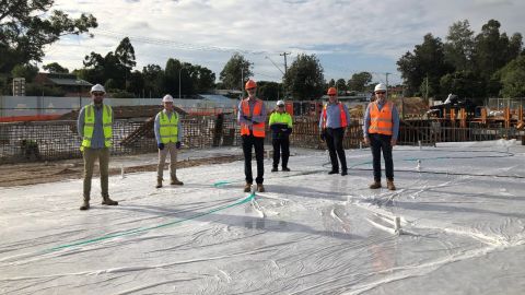 Six men in high-vis vests and hard hats stand on a concrete slab.