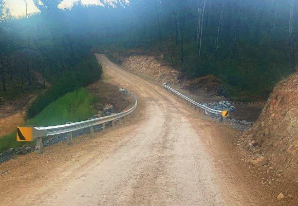 Image A dirt road lined with guardrail leads into a forested area.