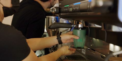 A close up shot of a barista holding a green cup making a coffee at a machine.