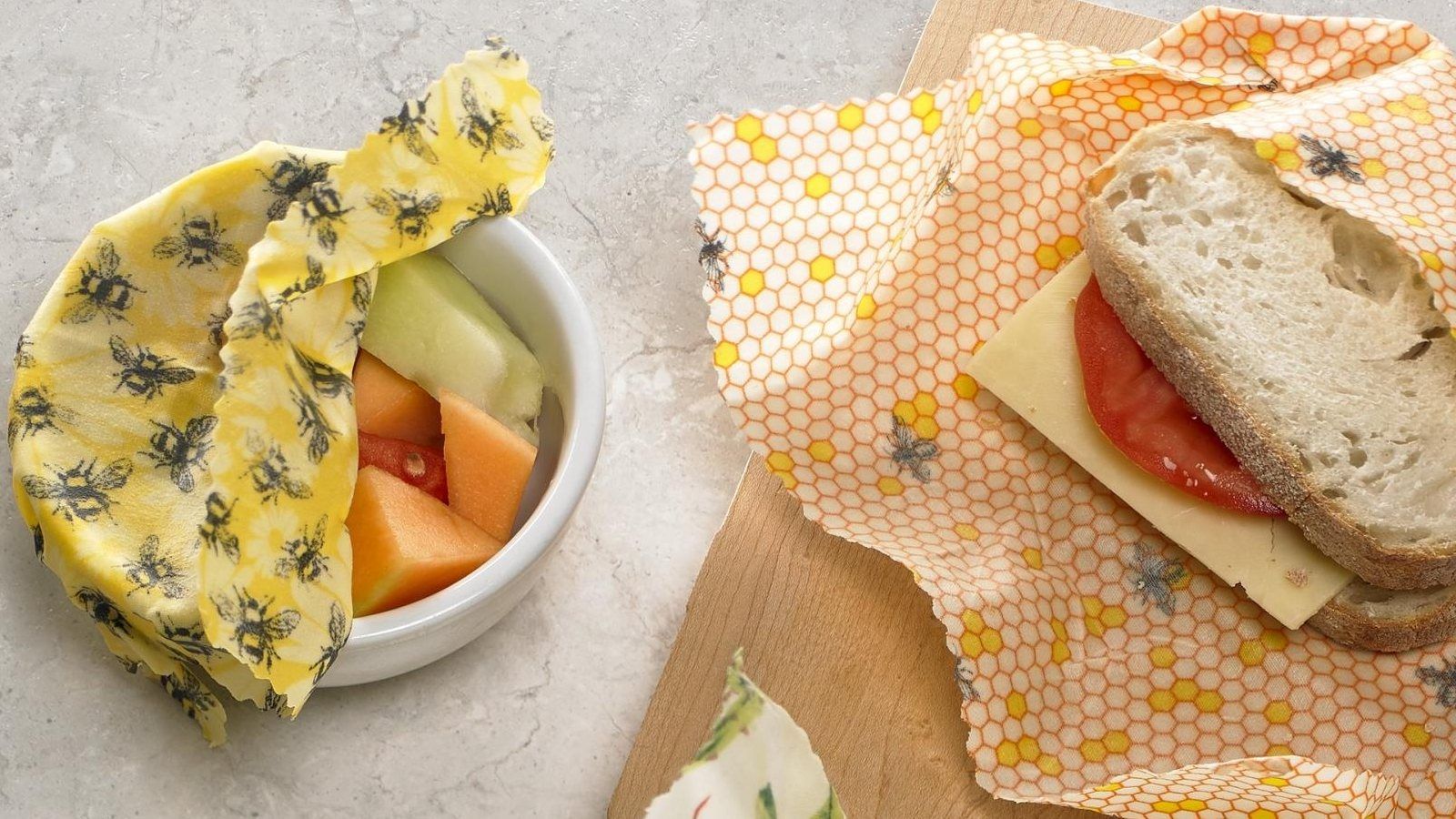 Close up image of bees wax wraps over food bowl with fruit and cheese and tomato sandwich banner image