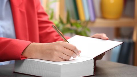 Close up of a person's hand about to write on the first blank page of a large book.
