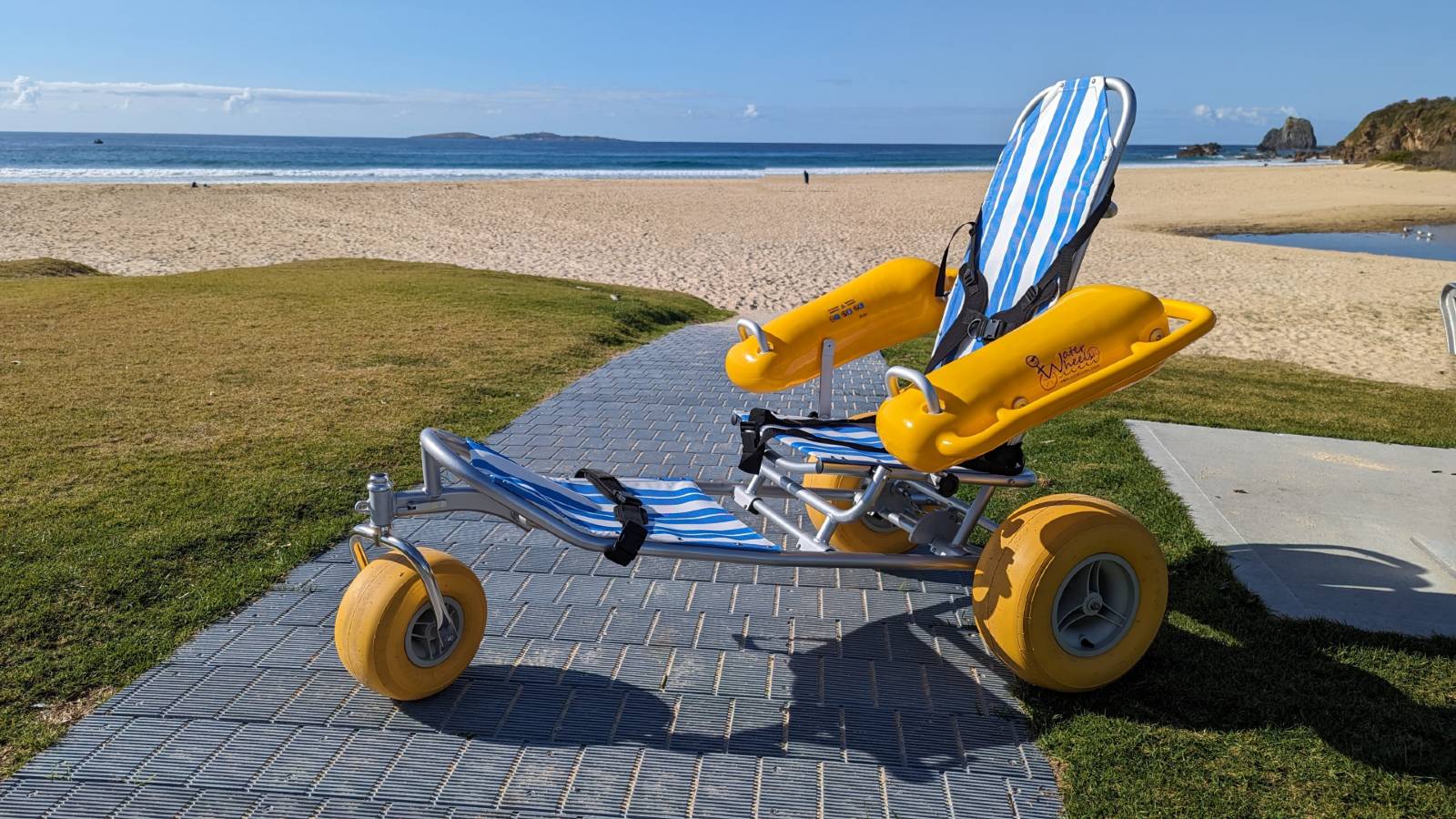 Image A floating beach wheelchair sitting at the edge of a sandy beach with a background of ocean and an island.