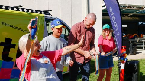 Four people cheer as the ribbon is cut in front of bright colourful van