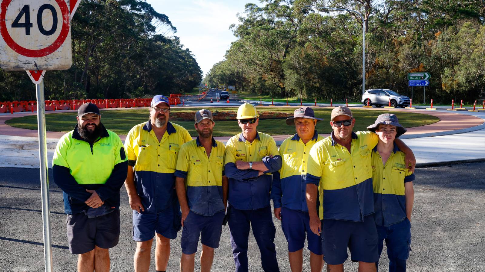 Image Road workers stand in a row in front of a roundabout under constrution